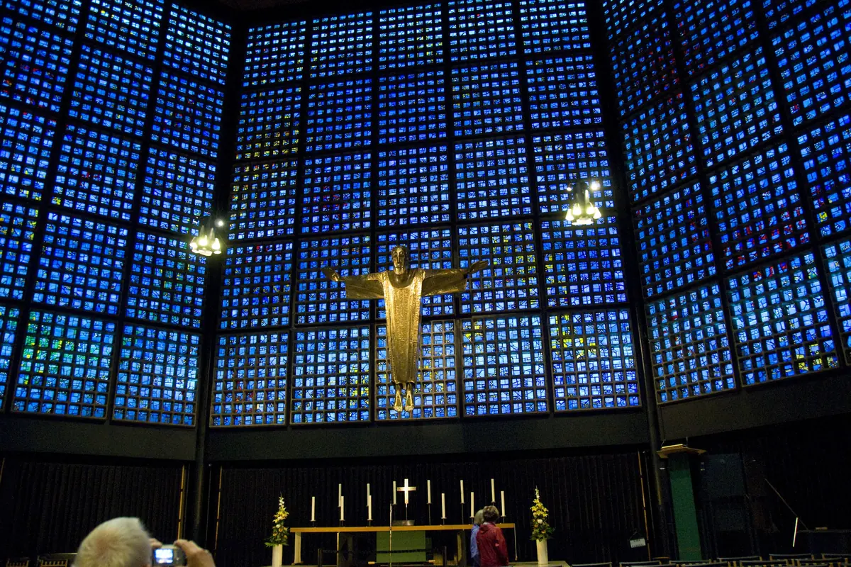 The blue glass wall of the Memorial Church nave rising behind the altar, with a gilt figure of Christ hanging in the middle of the wall and rows of wooden chairs in front