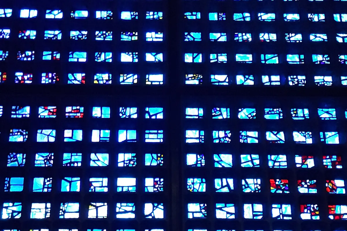 Close view of the nave wall of the Memorial Church, a grid of small blue glass panes in dark concrete frames with scattered red and white flecks