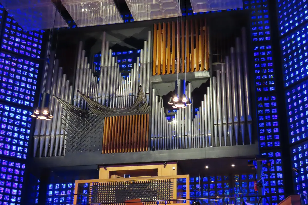 The organ of the Memorial Church seen from the floor of the nave: a grey and gold pipe case on a gallery framed by walls of small blue glass panes